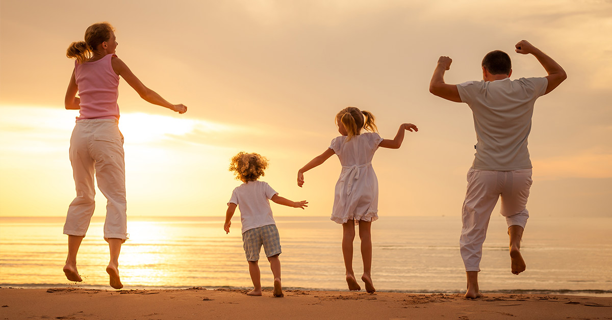 A family of four jumping and frolicking as the sun sets in the distance