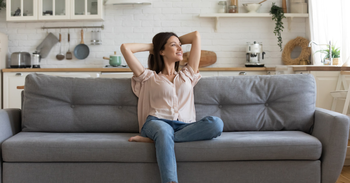 woman relaxing sitting int he middle of a couch with her arms up and hands clasped behind her head.