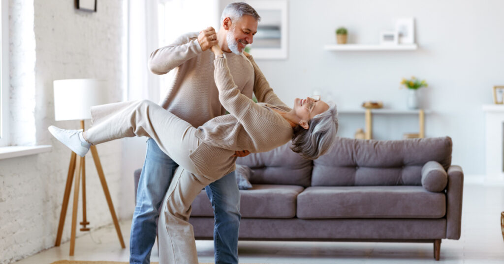 Older man dating an older woman having fun dancing in sitting room