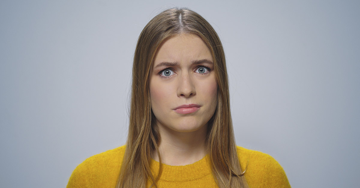 woman with dirty blonde hair with blue eyes looking confused wearing a yellow sweater