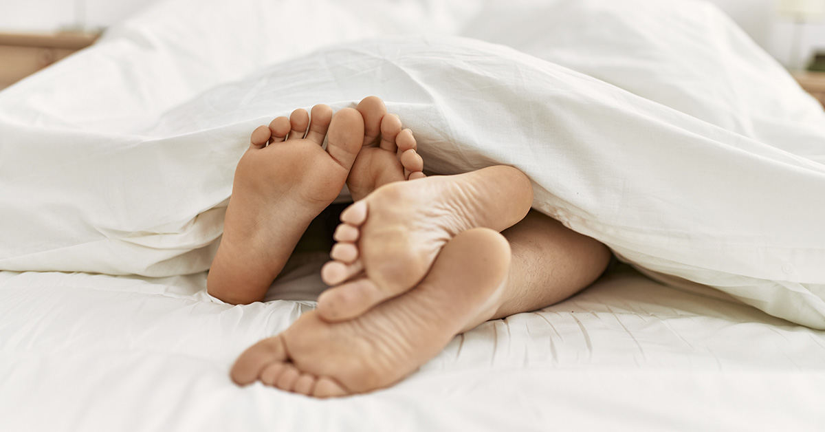 couples feet exposed from under bed sheets. Bedroom intimacy concept.