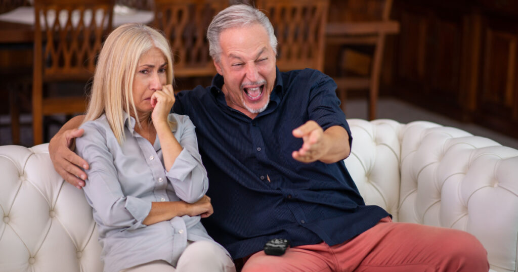 Man having a good laughter, his wife cries while watching the same tv program, lack of empathy concept