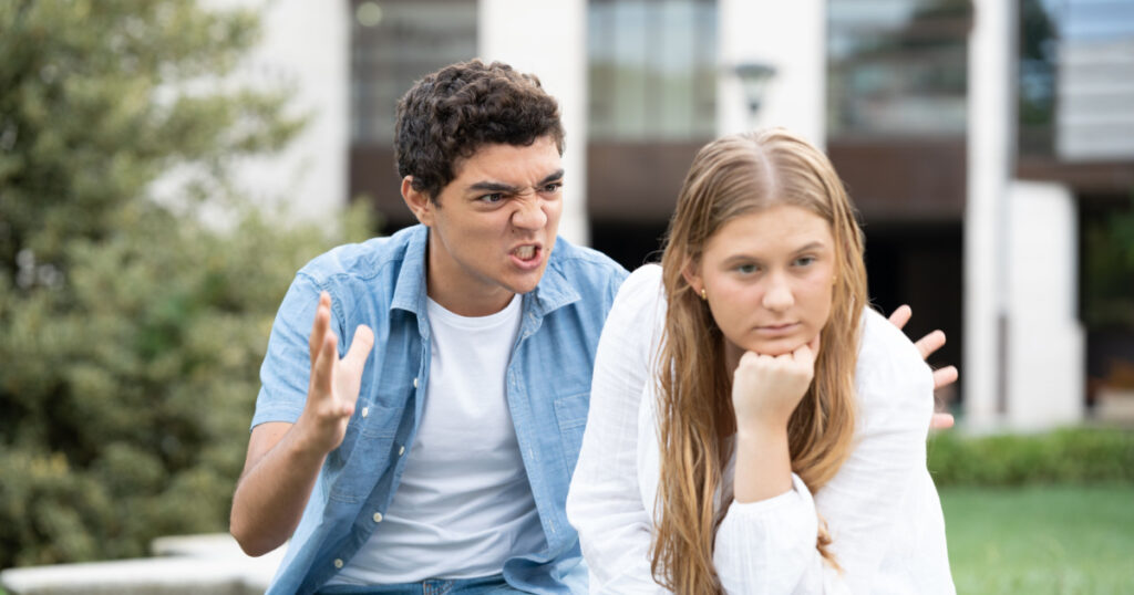 Angry and aggressive hispanic boy shouting and menacing girlfriend outdoors