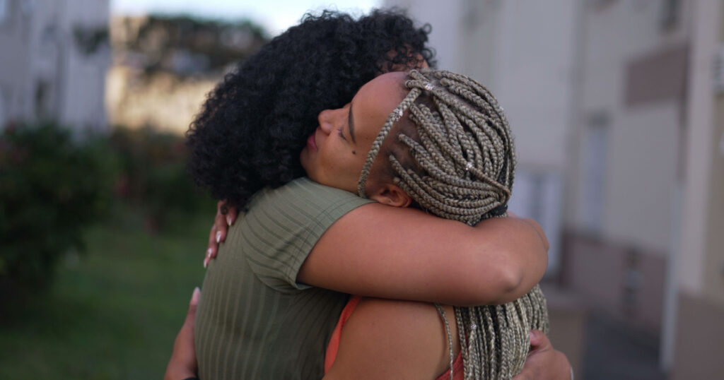 Two young black women hugging each other. Adult girlfriends embrace. People empath hug