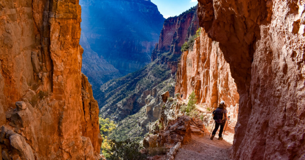 Hiker descends cliff edge trail in grand canyon's north rim, sunny day