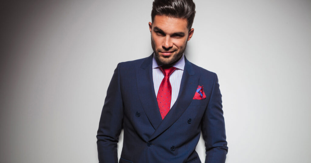 arrogant man with Narcissism with hands in pockets leaning against grey studio wall