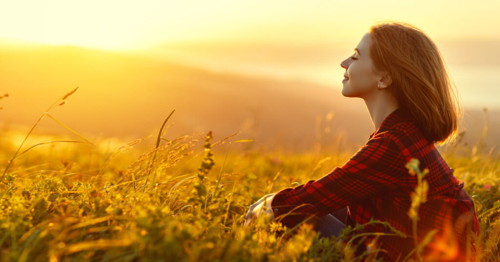 Woman sits with her back in the field and admires the sunset in the mountains
