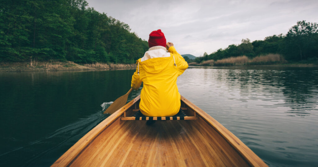 Rainy day boat ride. Rear view of woman in yellow raincoat paddling canoe. Active, adventure, outdoors, canoeing, kayaking 
