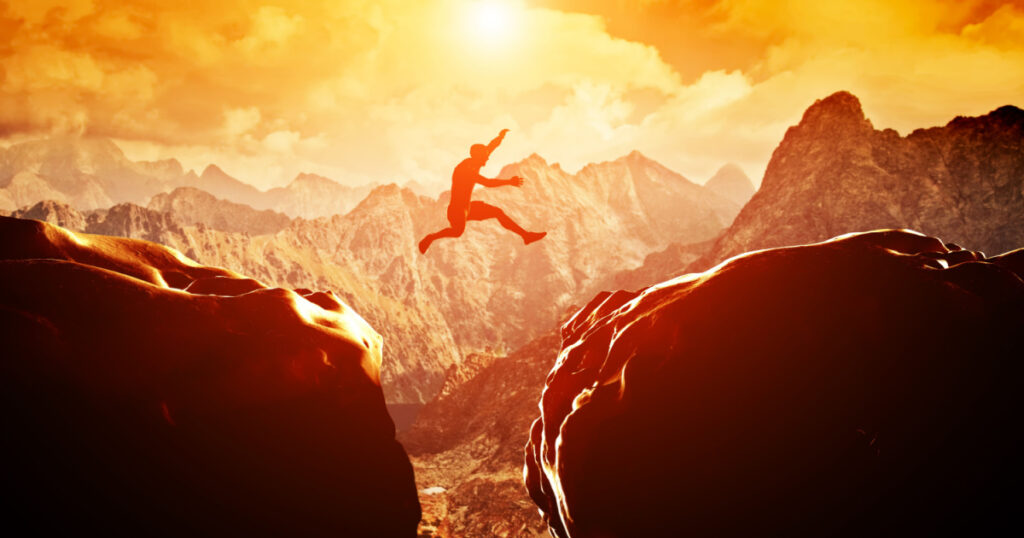 Man jumping over precipice between two rocky mountains at sunset. Freedom, risk, challenge, success.
