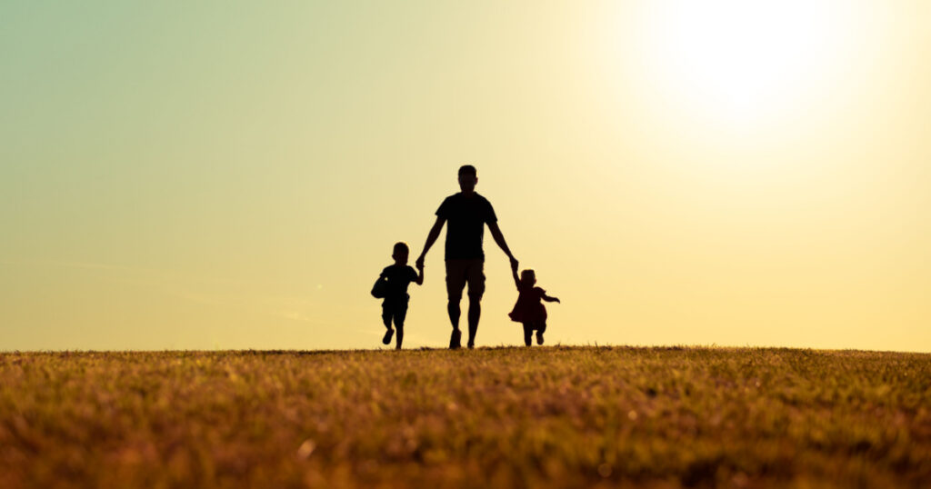 silhouette of father and children holding hands walking outdoors in the park. Fatherhood, and Father's Day concept. 