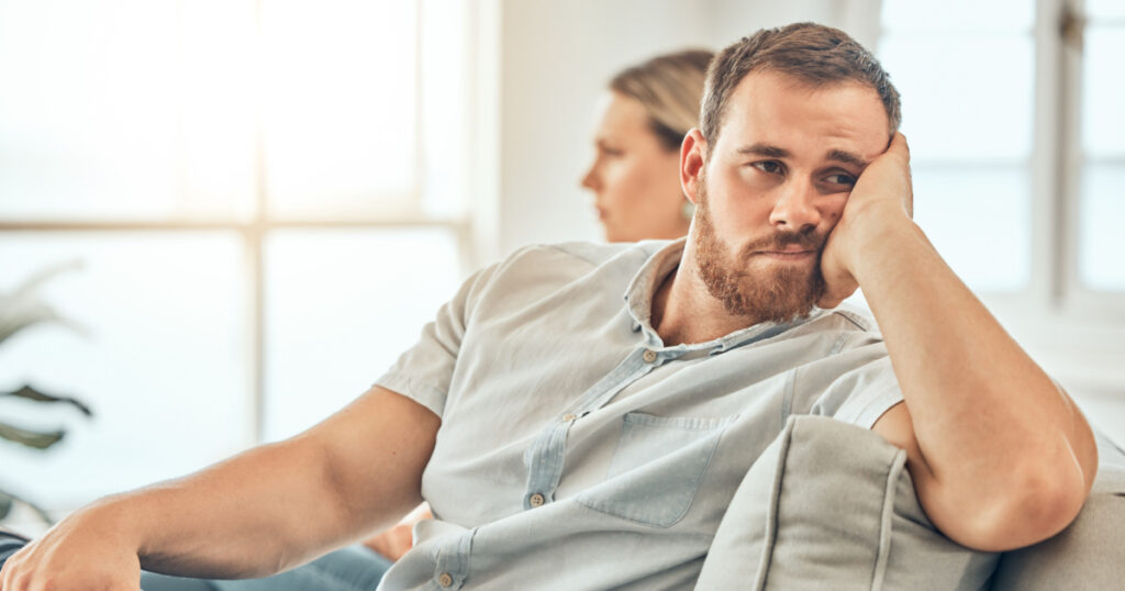 Young caucasian man with a beard looking unhappy and annoyed while sitting on the couch during an argument with his wife at home. Bored man sitting and thinking on the couch.