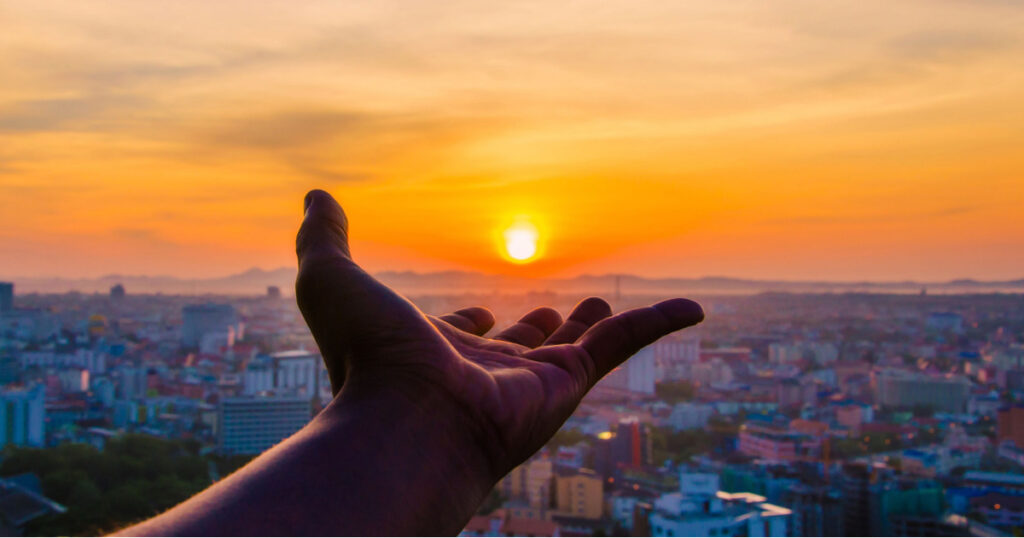 Hand holding sunset and city of background.
