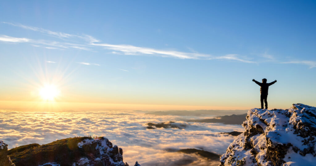 hiker celebrating success on top of a mountain in a majestic sunrise
