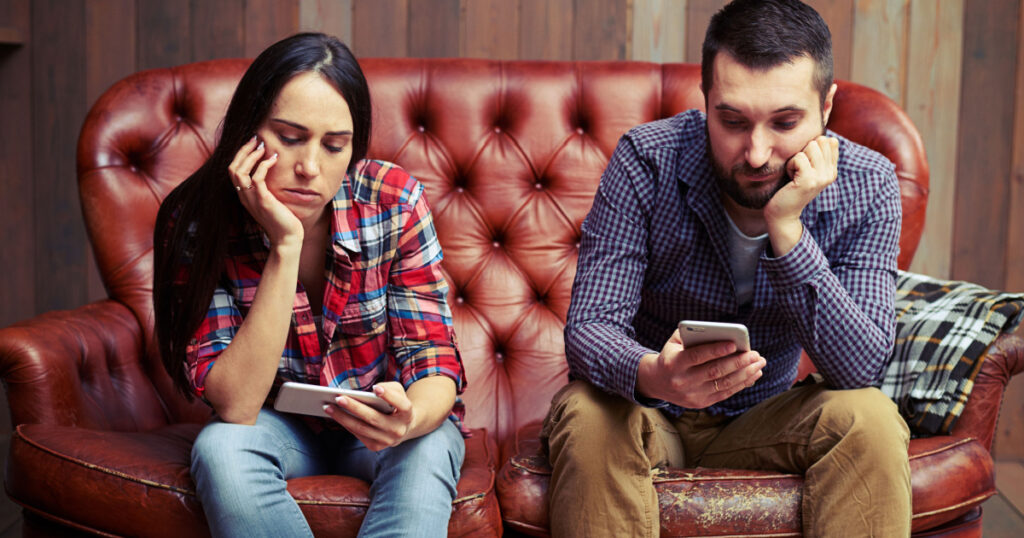 bored young couple sitting on couch and looking at their phones