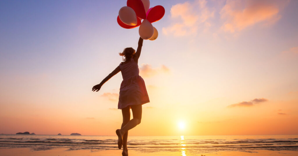 imagination, happy girl jumping with multicolored balloons at sunset on the beach, fly, follow your dream
