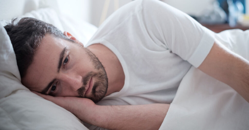Depressed man lying in his bed and feeling bad
