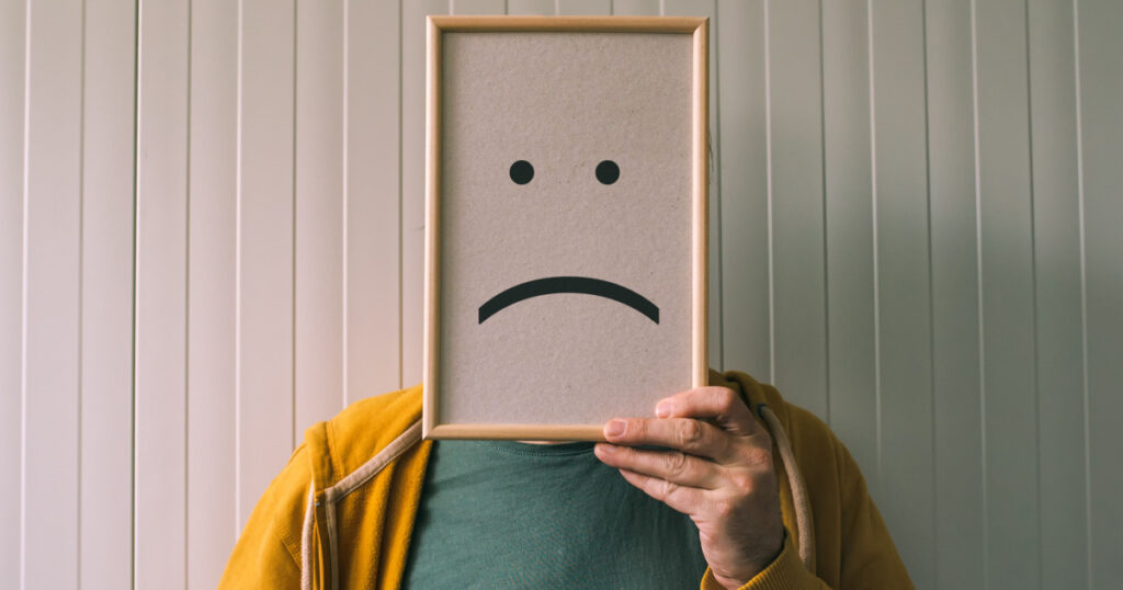 Put a sad pessimistic face on, sadness and depressive emotions concept, man holding picture frame with smiley emoticon printed.
