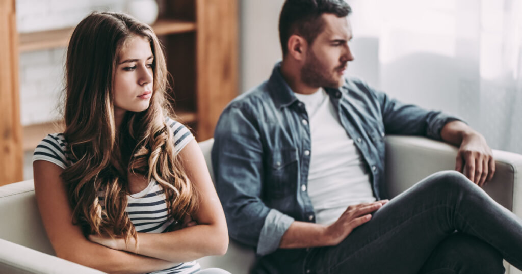 Upset couple at home. Handsome man and beautiful young woman are having quarrel. Sitting on sofa together. Family problems.