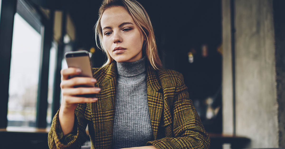 woman in greay turtleneck with brown jacket staring at smartphone in her hand