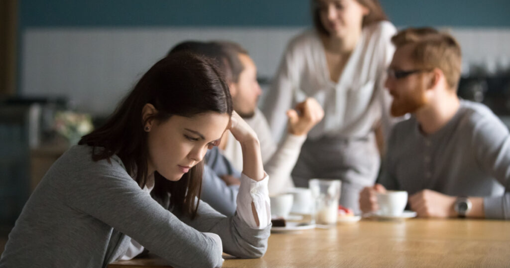 Upset young girl sit alone at coffee table in café feeling lonely or offended, sad female loner avoid talking to people, student outsider suffer from discrimination, lacking friends or company
