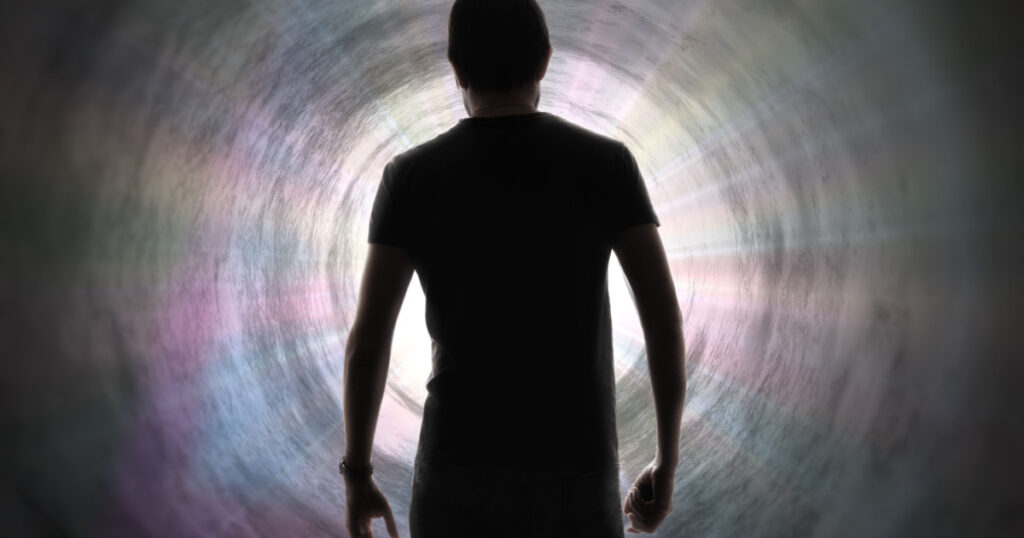 Silhouette of man's soul is going to bright light - rays of god inside tunnel. Life after death concept.
