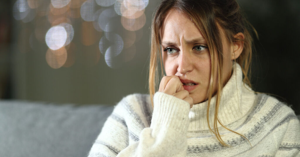 Nervous woman biting nails in winter sitting on a couch in the night at home

