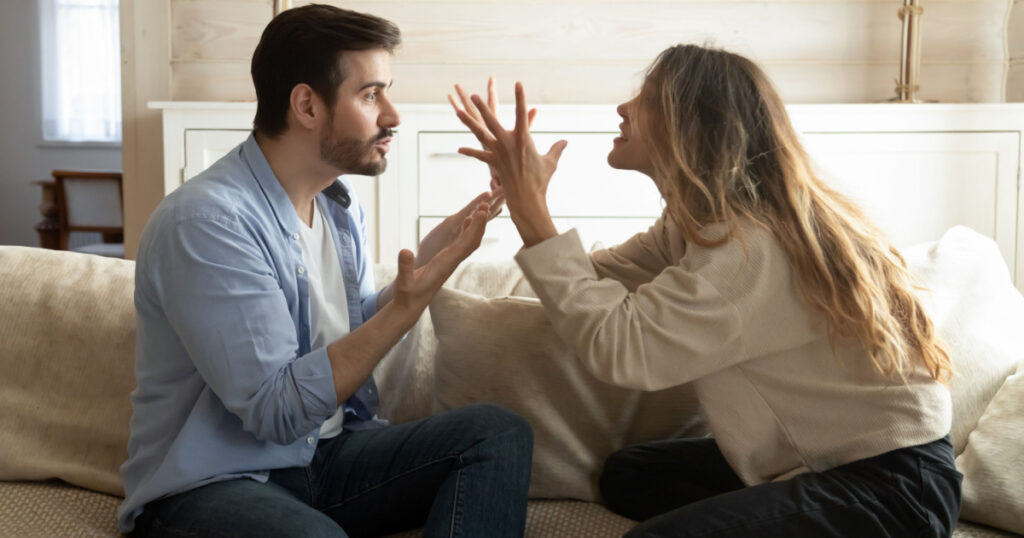 Emotional annoyed stressed couple sitting on couch, arguing at home. Angry irritated nervous woman man shouting at each other, figuring out relations, feeling outraged, relationship problems concept.
