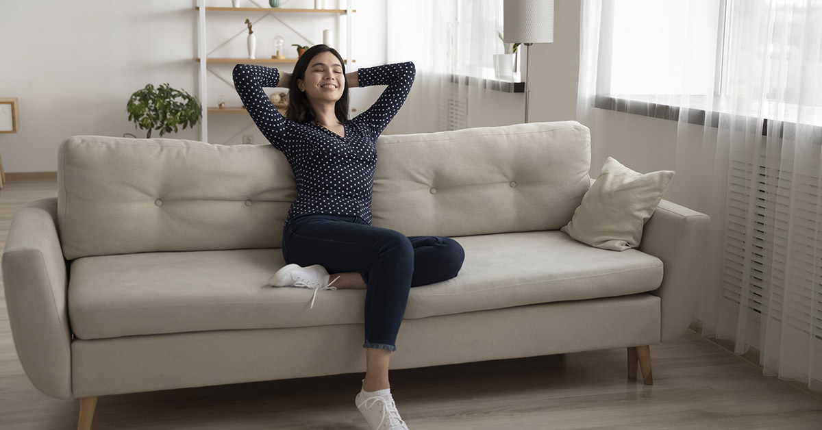 woman relaxing with hands behind head sitting in the center of a couch