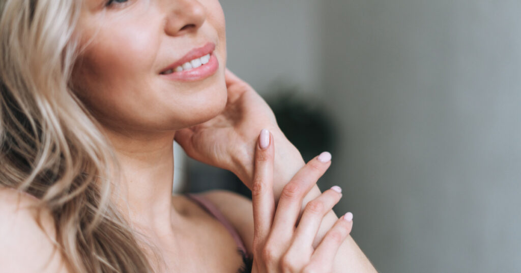 Beauty portrait of blonde smiling woman 35 year plus clean fresh face and hands with light pink manicure
