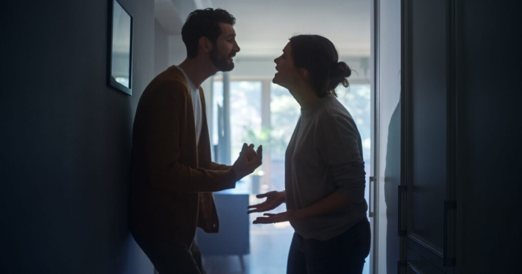 Young Couple Arguing and Fighting. Domestic Violence and Emotional abuse Scene, Stressed Woman and aggressive Man Screaming at Each other in the Dark Hallway of Apartment. Dramatic Scene
