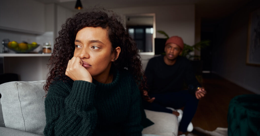 Multi-cultural female ignoring black boyfriend while fighting on the sofa in modern apartment
