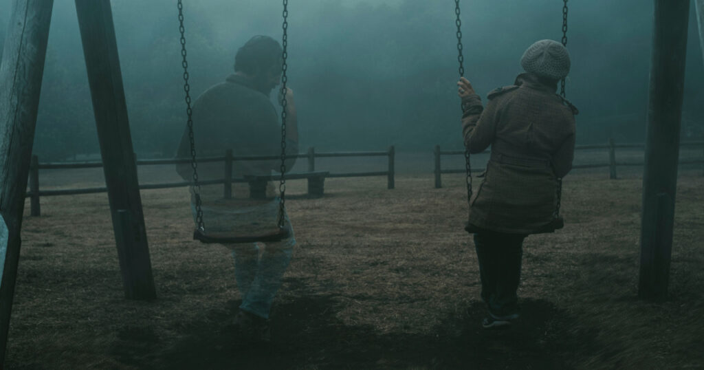 Concept of afterlife and memory for parents or lost love. Back view of woman sitting on a swing with ghost man near her outdoor in the park with fog. . Dead friend or husband concept. Life and death
