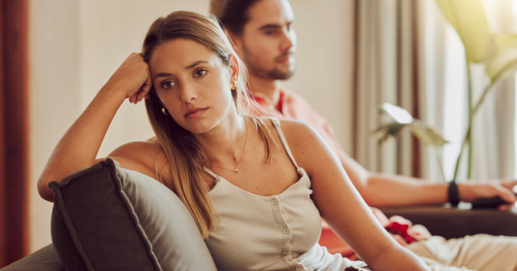 Unhappy, sad and annoyed couple after a fight and are angry at each other while sitting on a couch at home. A woman is stressed, upset and frustrated by her boyfriend after an argument
