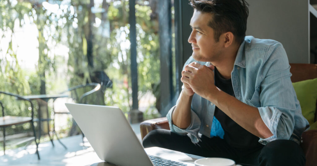 Asian handsome man sitting happily looking out of the window in a cafe. Concept freelance and financial freedom.
