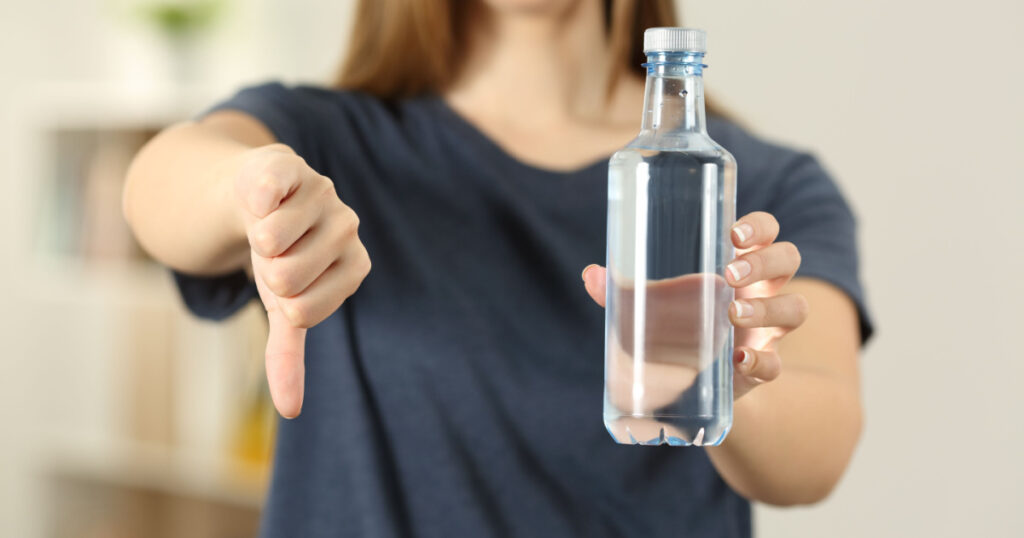 Front view close up of a woman hands holding a bottle of water with thumbs down at home
