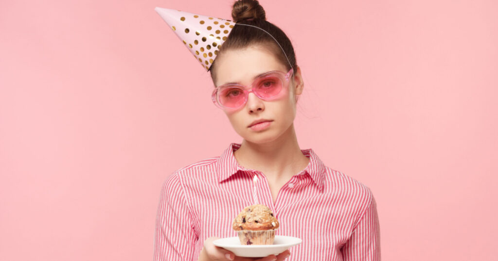 Unhappy birthday woman holding plate with holiday cake and looking at it with sad face, tired of party, isolated on pink background
