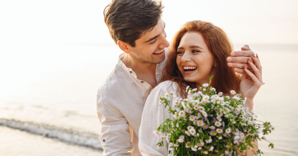 Young fun surprised couple family man woman in white clothes rest relax together boyfriend meet girlfriend close eyes gift give bouquet flowers at sunrise over sea beach outdoor seaside in summer day
