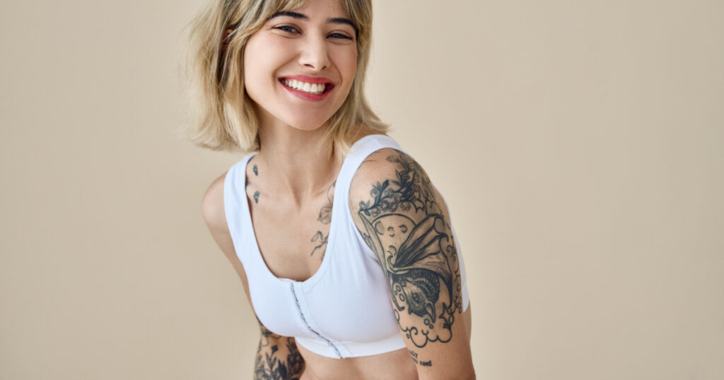 Smiling blond pretty happy girl beauty female generation z tattooed model with short blonde hair beautiful face healthy skin looking at camera laughing isolated at beige background. Aesthetic portrait
