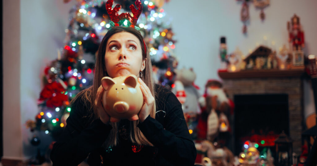 Broke Woman Holding a Piggy Bank Regretting Christmas Spendings. Desperate girl feeling sad about spending too much money on holidays
