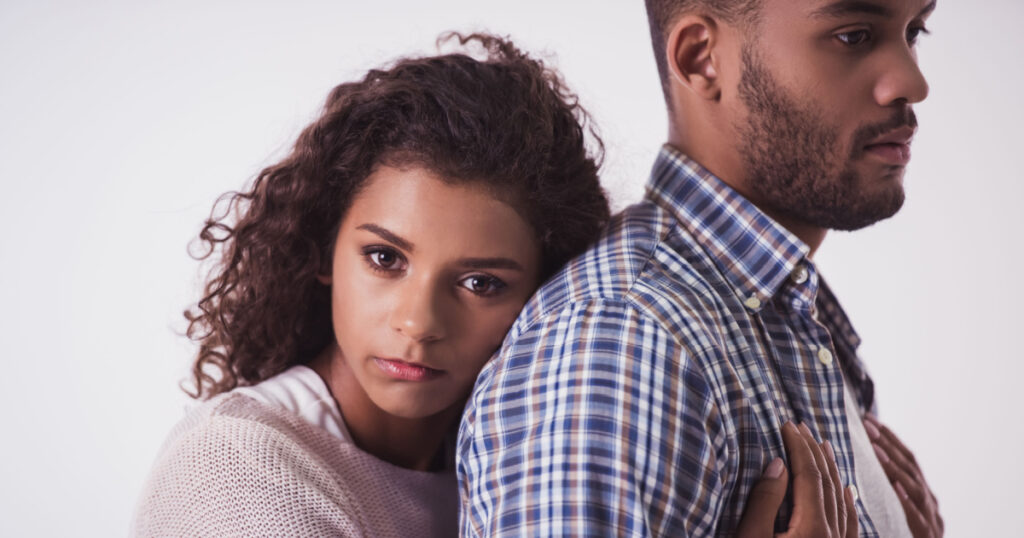 Beautiful Afro American girl is hugging her handsome guy and looking sadly at camera, isolated on white
