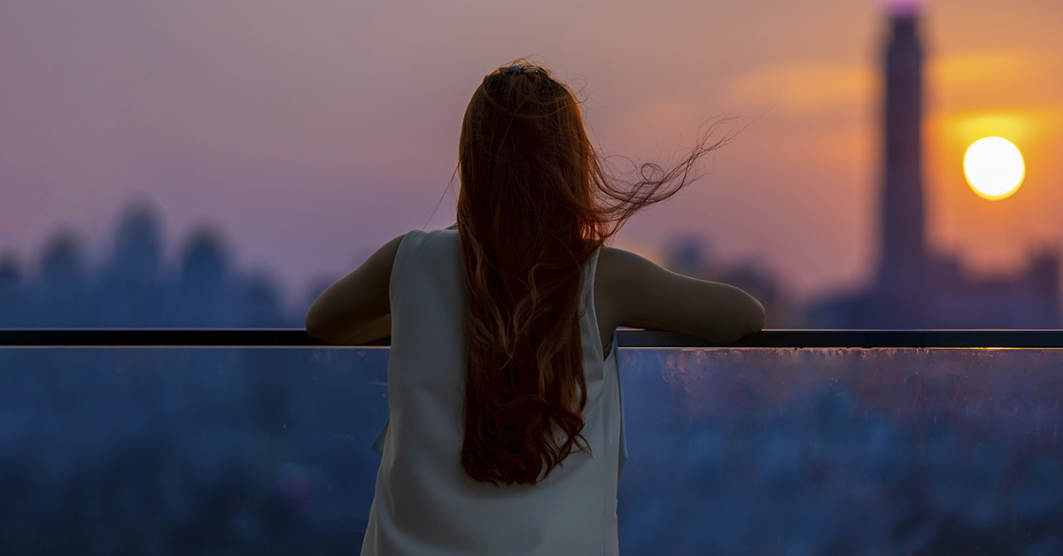 woman seen from behind looking into distance at sunset. City setting. Contemplation concept