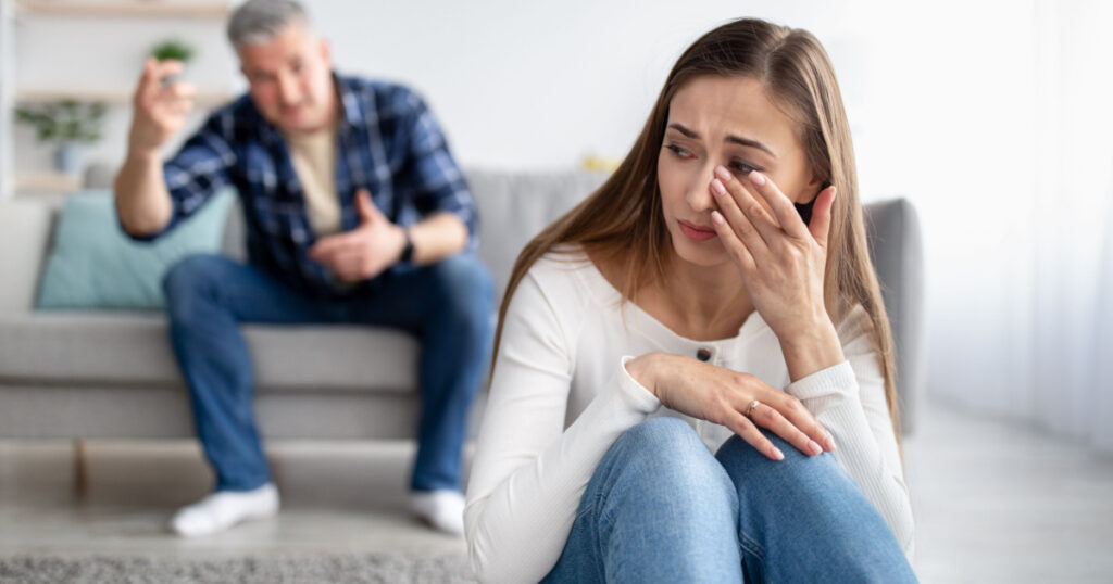 Emotional or psychological domestic violence concept. Mature man abusing his depressed wife, shouting, humiliating and threatening her, middle aged woman crying on floor at home
