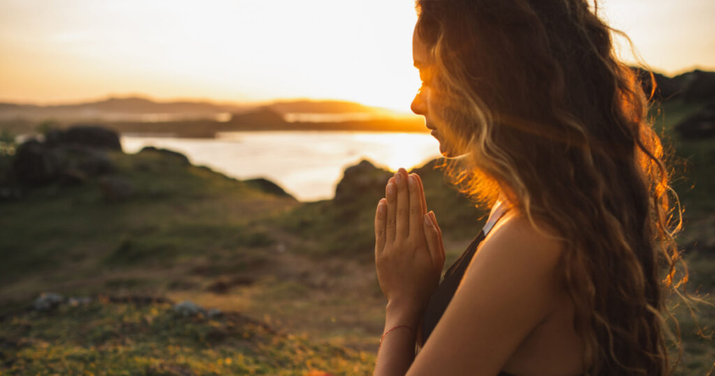 Woman praying alone at sunrise. Nature background. Spiritual and emotional concept. Sensitivity to nature
