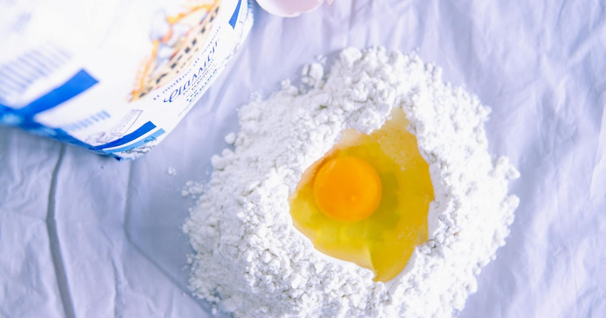 A fresh egg nestled in flour, ready for homemade pasta preparation, flat lay.