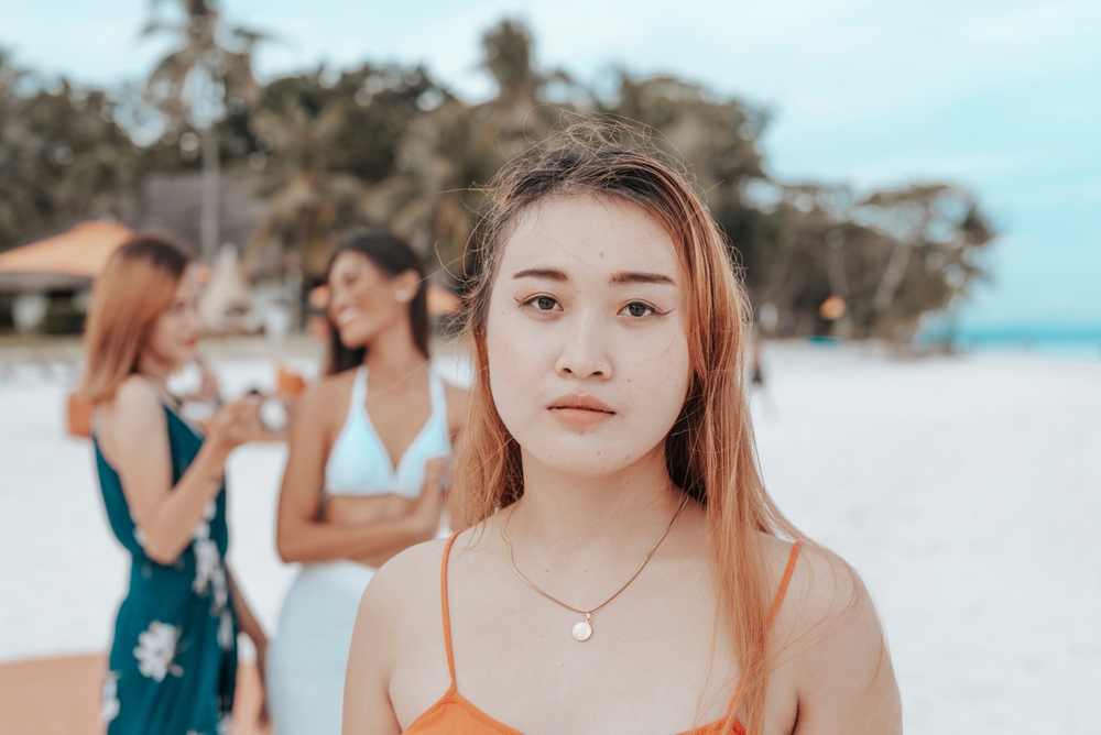 A depressed young woman realizing her 2 friends talking and gossiping behind her back, realizing their fake friendship. Outdoor beach scene.