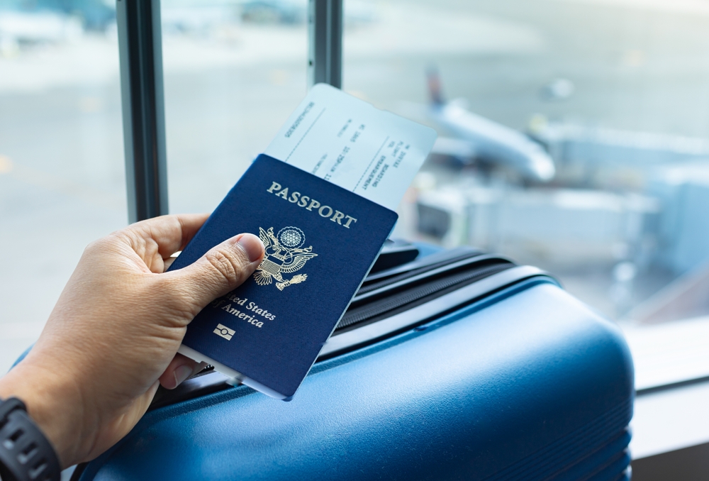 American passport and plane ticket in hand over suitcase