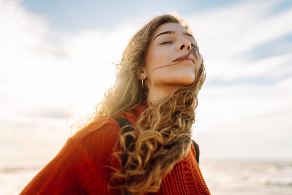 Portrait of a beautiful woman with backpack on the beach in cold weather. Autumn near the sea. Calmness and tranquility. Travel, tourism concept.