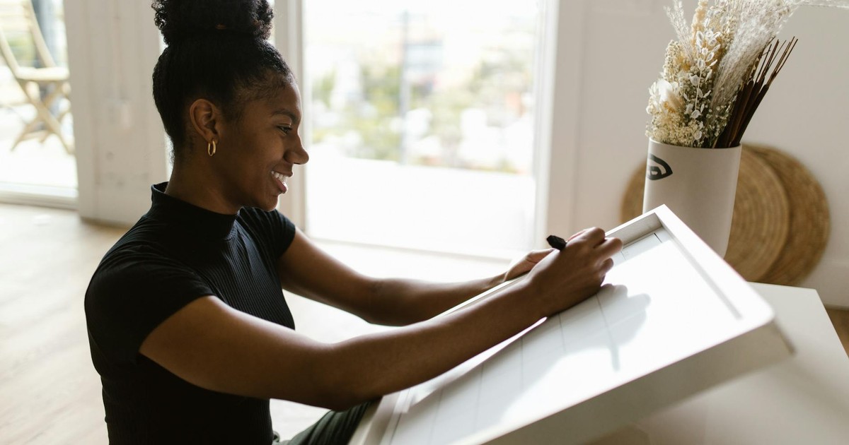 A woman sits indoors writing on a whiteboard, planning her ideas while enjoying the natural light.