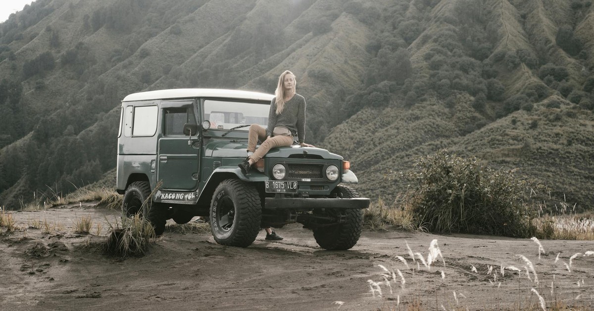 A woman sits on a jeep in a rugged mountain landscape.