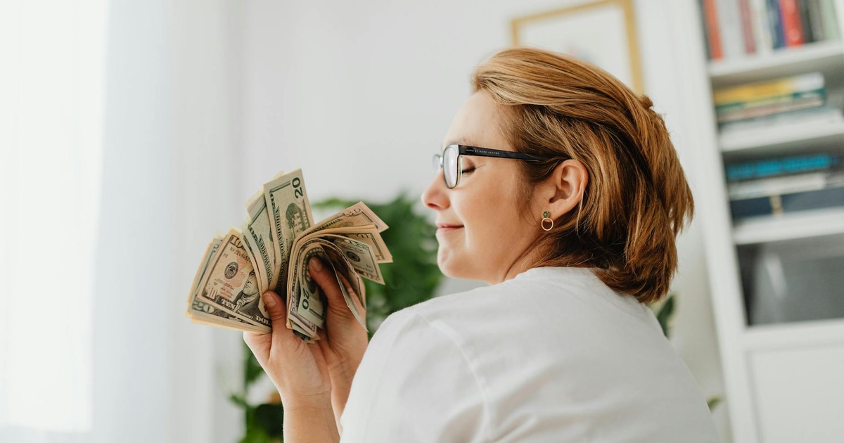 Confident woman in glasses holding US dollar bills, symbolizing wealth and finance.